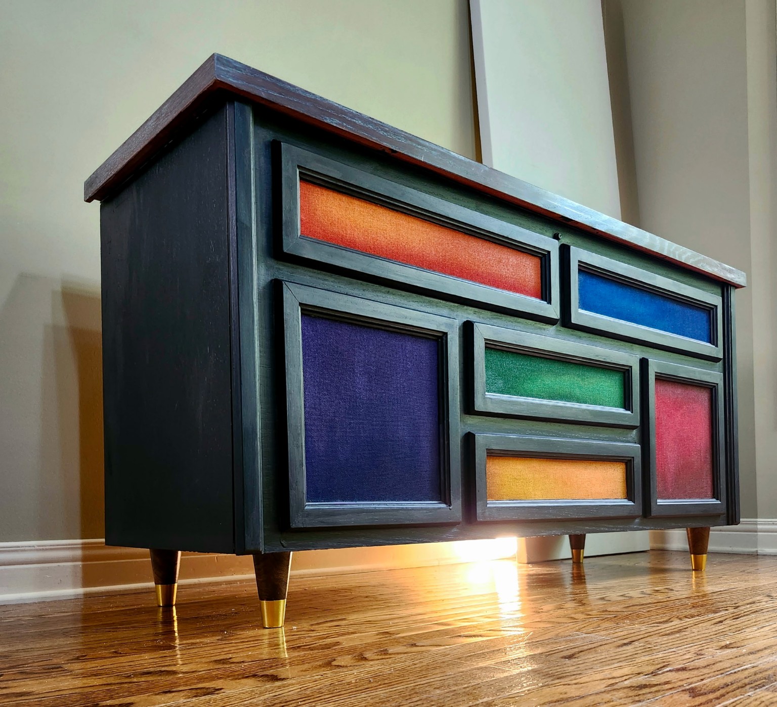 Sculptural dark console with colourful geometric inset panels and brass-tipped legs